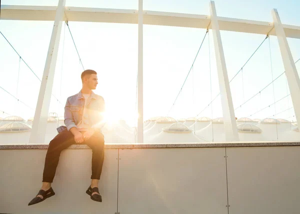 Cara de moda sentado ao pôr do sol posando em óculos de sol — Fotografia de Stock