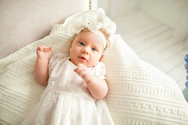 Kleines Mädchen mit weißer Schleife liegt auf dem Sofa, auf weißem Hintergrund. — Stockfoto