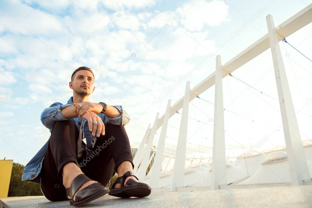 fashion guy sitting at sunset posing 