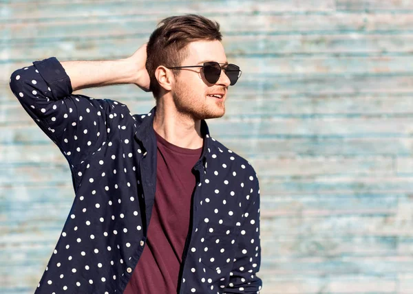Fashion guy in glasses poses near a wooden wall in blue — Stock Photo, Image