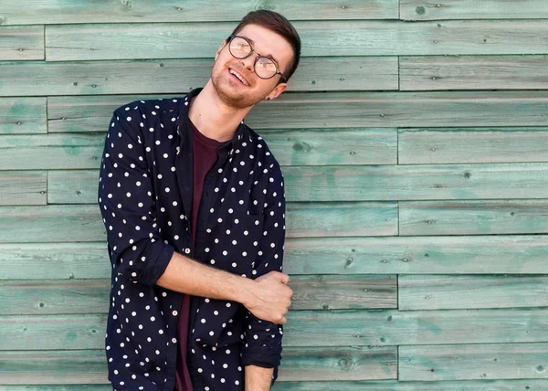 Modetyp Hipster mit Modebrille posiert auf einem hölzernen blauen Hintergrund — Stockfoto