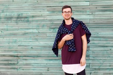 Gözlüklü moda adam mavi ahşap bir duvarının yakınında poz veriyor