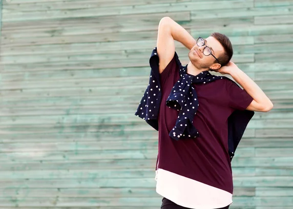 Fashion guy in glasses poses near a wooden wall in blue — Stock Photo, Image