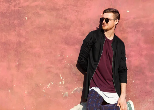 Fashion guy in glasses stands near a crumpled concrete wall with cracked paint — Stock Photo, Image