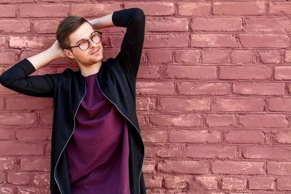 Cara de moda em óculos fica perto de uma parede de tijolo com tinta rachada — Fotografia de Stock