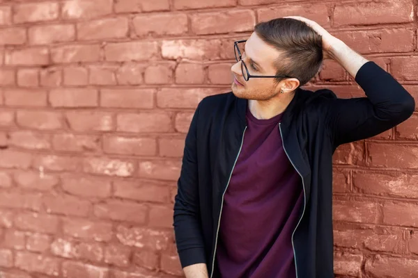 Mode killen i glasögon står nära en tegelvägg med sprucken färg — Stockfoto