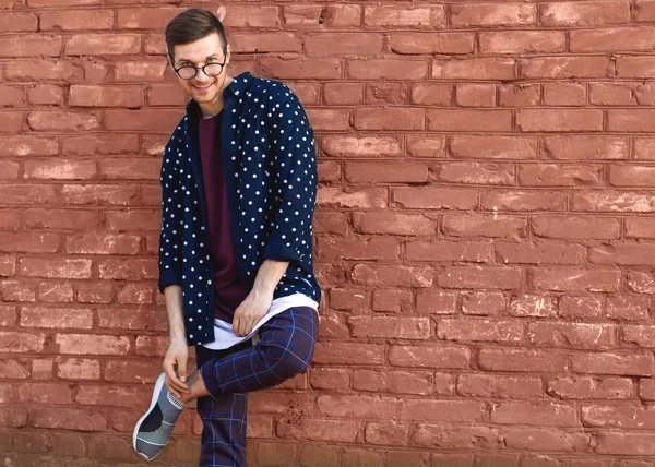 戴眼镜的时尚家伙站在一堵砖墙旁边, 油漆开裂。 — 图库照片