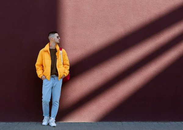 Fashion guy en lunettes de soleil et une veste jaune posant près du mur lilas — Photo