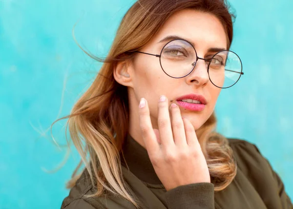 Fashion girl in round glasses stands posing near a turquoise wal — Stock Photo, Image