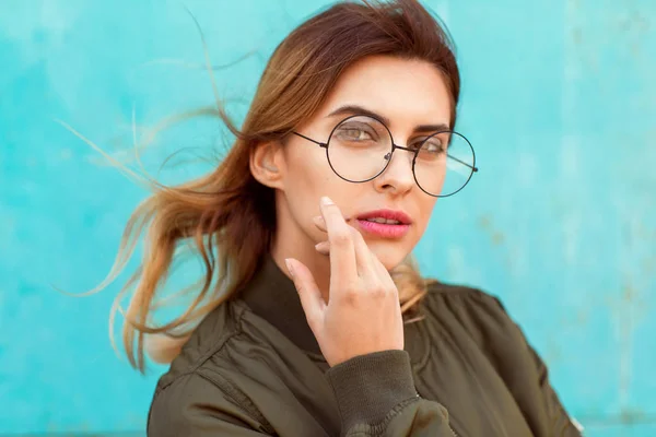 Fashion girl in round glasses stands posing near a turquoise wal — Stock Photo, Image