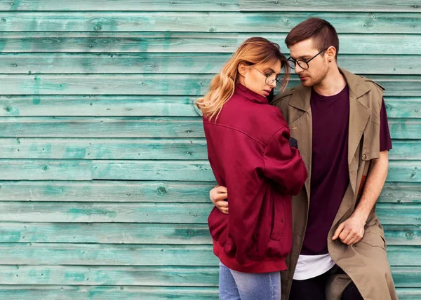 Couple de mode dans leurs lunettes avec des vêtements bordeaux posant sur un mur en bois bleu — Photo