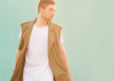 Gözlüklü moda adam duvara yakın ekşi dalga rengini günbatımında pozlar