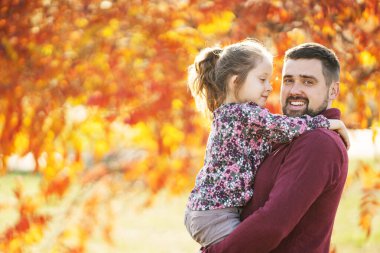 Baba kızıyla birlikte sonbahar parkında yürüyor.