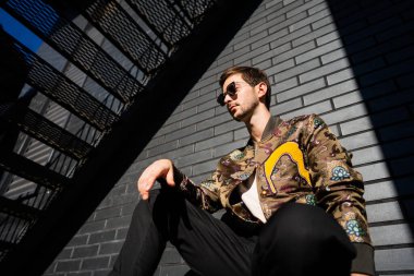 Şehir merkezinde siyah tuğlalı bir duvarda poz veren moda adamı.