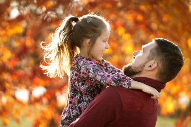 Baba kızıyla birlikte sonbahar parkında yürüyor.