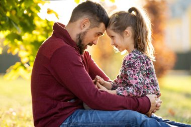 Baba kızıyla birlikte sonbahar parkında yürüyor.