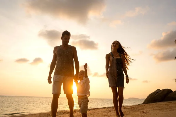 Aile gün batımında mutlu bir şekilde tropik bir plajda yürüyor. — Stok fotoğraf