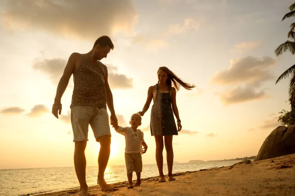 Aile gün batımında mutlu bir şekilde tropik bir plajda yürüyor. — Stok fotoğraf