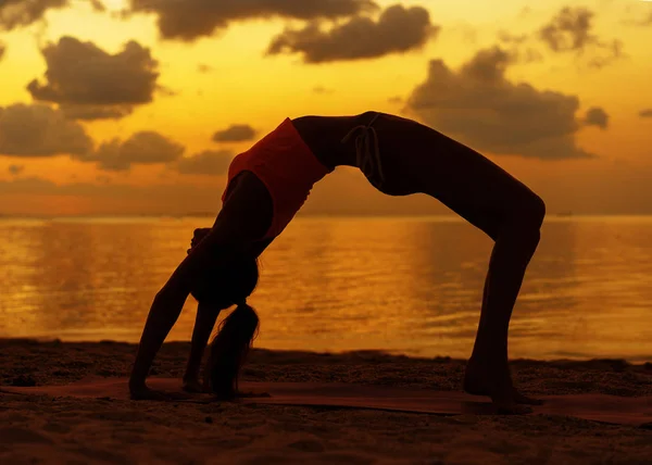 Chica haciendo yoga en la playa al atardecer —  Fotos de Stock