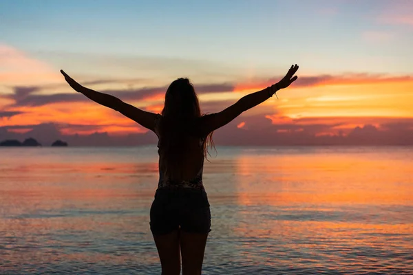 Mädchen bei Sonnenuntergang steht am Meer und hebt die Hände — Stockfoto