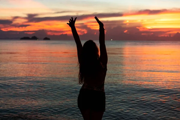 해가 지는 곳에 서 있는 소녀는 손을 들어 자유를 얻는다 — 스톡 사진