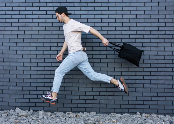 Cara de moda pulando contra parede de tijolo preto com compras, compras — Fotografia de Stock