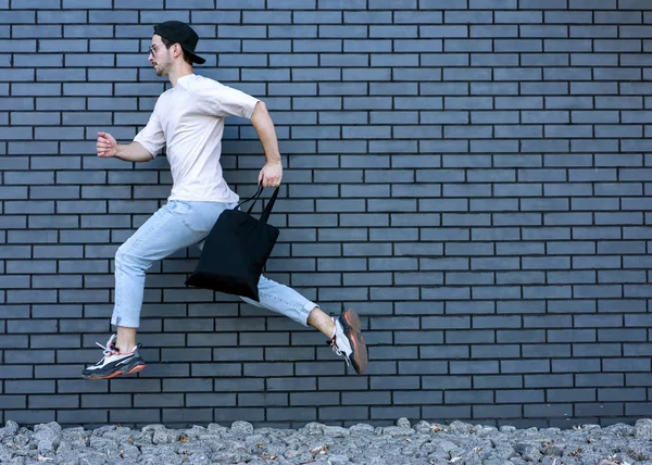 Cara de moda pulando contra parede de tijolo preto com compras, compras — Fotografia de Stock