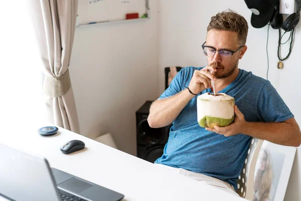 Na volné noze sedí v kanceláři a pracuje a pije kokos — Stock fotografie