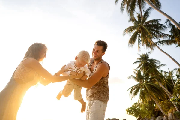 Família feliz caminhar ao longo de uma praia tropical ao pôr do sol — Fotografia de Stock