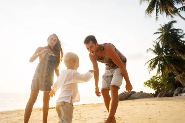 Familia feliz caminar a lo largo de una playa tropical al atardecer — Foto de Stock