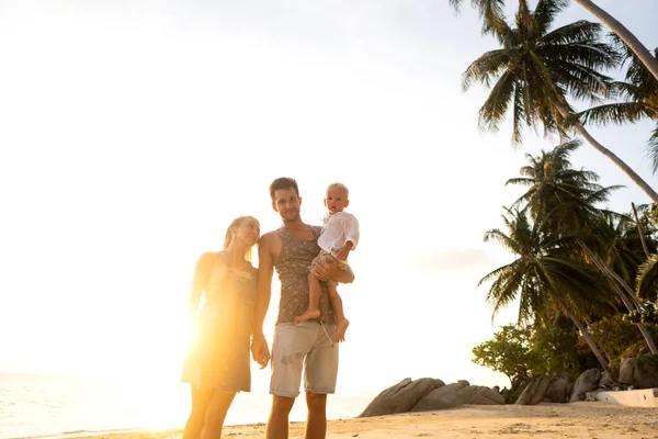 Aile gün batımında mutlu bir şekilde tropik bir plajda yürüyor. — Stok fotoğraf
