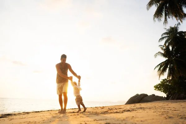 Μπαμπάς με ένα παιδί στο ηλιοβασίλεμα στην παραλία διασκεδάζοντας και γυρίζοντας — Φωτογραφία Αρχείου