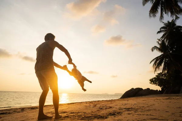 Pai com uma criança ao pôr do sol na praia se divertindo e girando — Fotografia de Stock