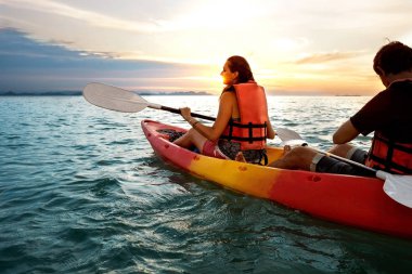 Çift birlikte kayak yapıyor. Güzel genç bir çift gölde kayak yapıyor ve gün batımında gülümsüyor.