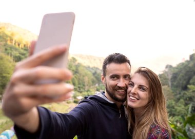 Birkaç turist gün batımında Tayland dağlarında selfie çekiyor.