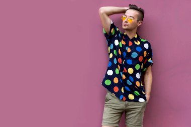 Eski moda gözlüklü duygusal adam eski moda elbiseli pembe bir duvara karşı duruyor.