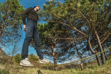 Sakal ve giyen güneş gözlüğü, yaşlı bir adam, bir slackline günbatımında iki ağaç arasında açık havada dengeler