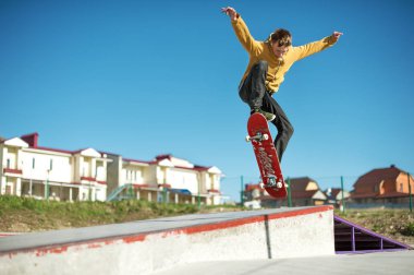 A teenager skateboarder does an ollie trick in a skatepark on the outskirts of the city clipart