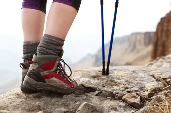 Nahaufnahme weiblicher Beine in Trekkingstiefeln mit Stöcken für Nordic Walking vor dem Hintergrund von Felsen und fernen kaukasischen Ländern — Stockfoto