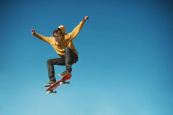 Un skateboarder adolescente hace un truco ollie en el fondo de gradiente cielo azul — Foto de Stock