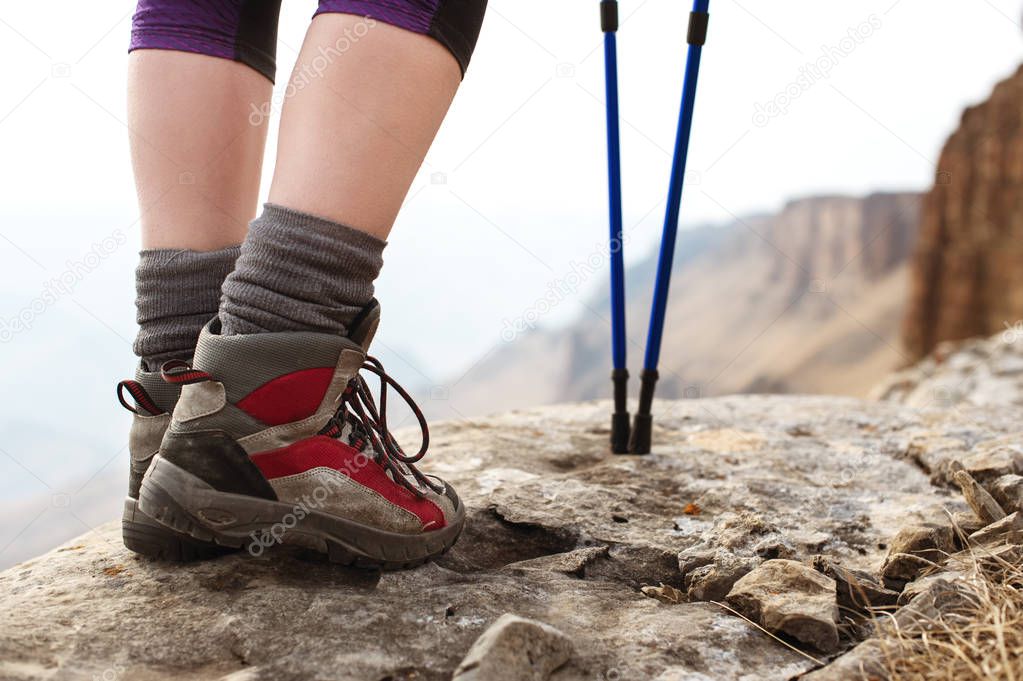 Close-up of female legs in trekking boots with sticks for Nordic walking against the background of rocks and distant Caucasian lands