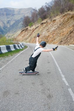 Güzel dağ manzarası zemin karşı dağlarda bir dağ yolu üzerinde iken serpantin hızda stand-up bir slayt Longboarder tulum kask ve eldiven longboard üzerinde gerçekleştirir