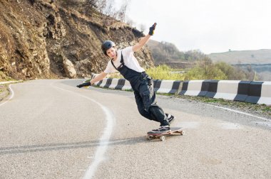 Güzel dağ manzarası zemin karşı dağlarda bir dağ yolu üzerinde iken serpantin hızda stand-up bir slayt Longboarder tulum kask ve eldiven longboard üzerinde gerçekleştirir