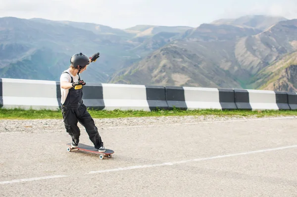 Longboarder auf Longboard in Overalls Helm und Handschuhen führt eine Stand-up-Rutsche mit Geschwindigkeit, während auf einer Bergstraße Serpentine in den Bergen vor der Kulisse einer schönen Berglandschaft — Stockfoto