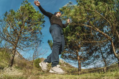Sakal ve giyen güneş gözlüğü, yaşlı bir adam, bir slackline günbatımında iki ağaç arasında açık havada dengeler