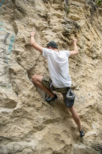 Молодой человек занимается скалолазанием по крутой скале без страховки — стоковое фото