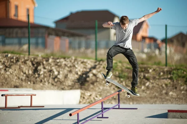 Nastoletnia skater w szary T-shirt i słuchawki i dżinsy ślizga się przez Reling na deskorolce w skate park — Zdjęcie stockowe