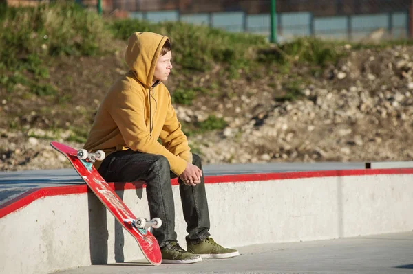 Підліток сидить у жовтому светрі зі скейтбордом на тлі міського нетря — стокове фото