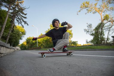 Bir genç adam eylem bir slayt bir longboard üzerinde şehrin tesisi alanı yapar.