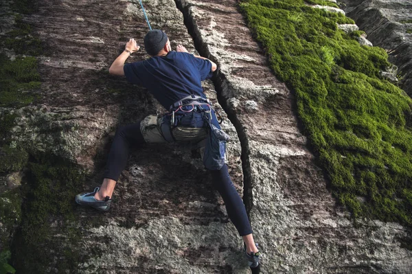 Молодой хипстер занимается скалолазанием со страховкой на скалах с зеленым мхом — стоковое фото